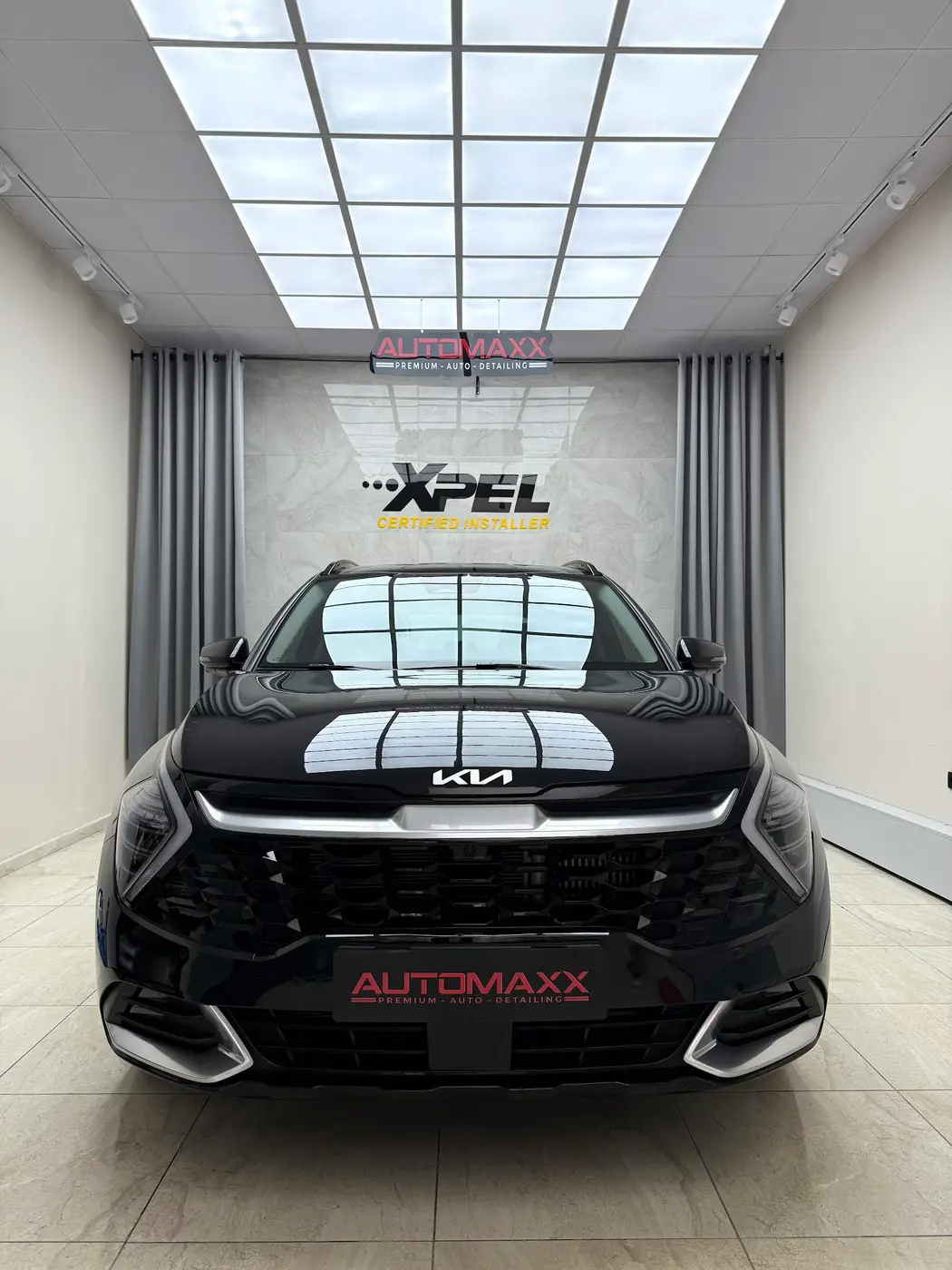 Automaxx atölyesinde, XPEL Certified Installer duvarının önünde duran siyah Kia SUV