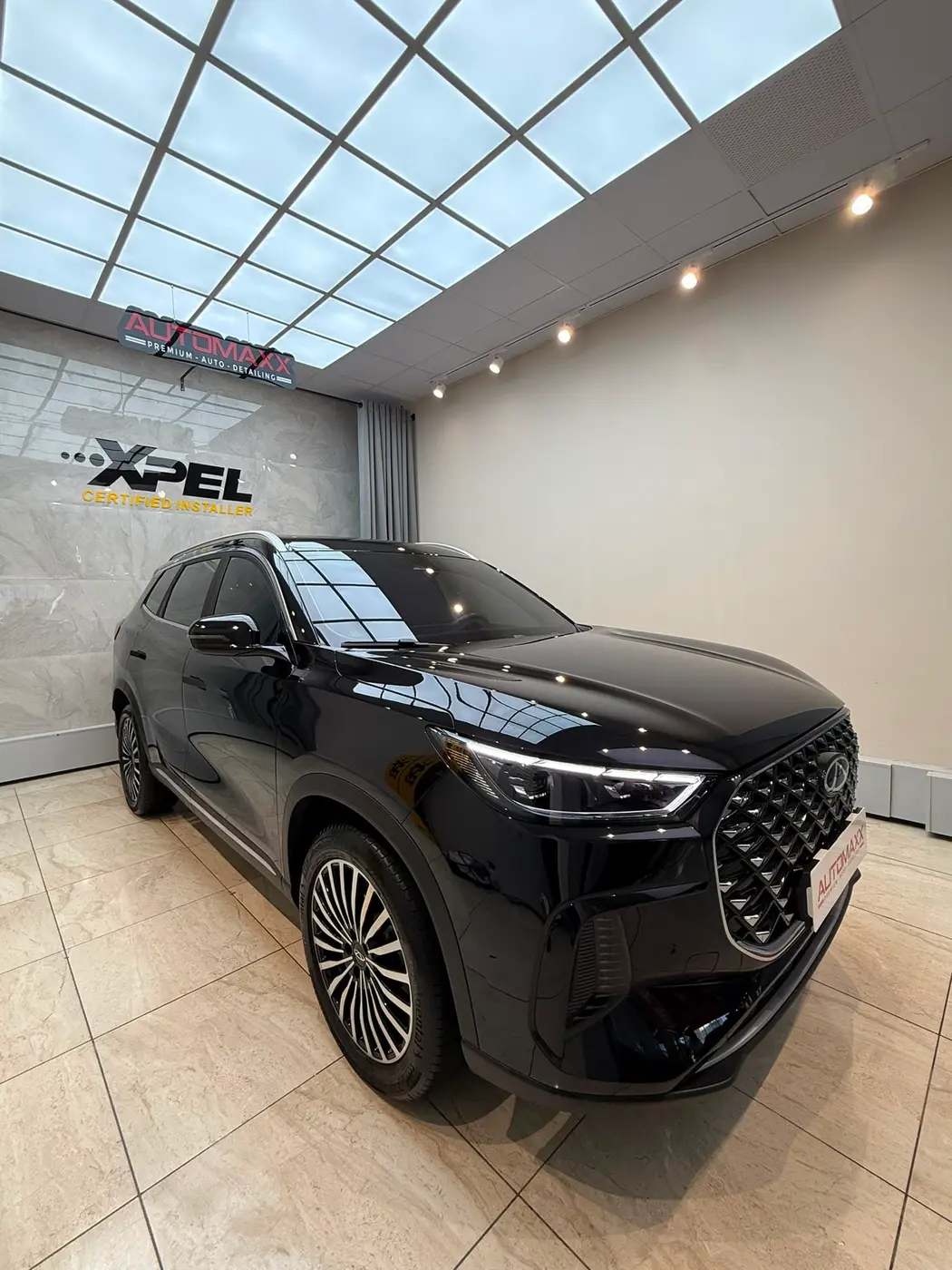 Automaxx atölyesinde parlak siyah SUV; arkada XPEL Certified Installer duvarı