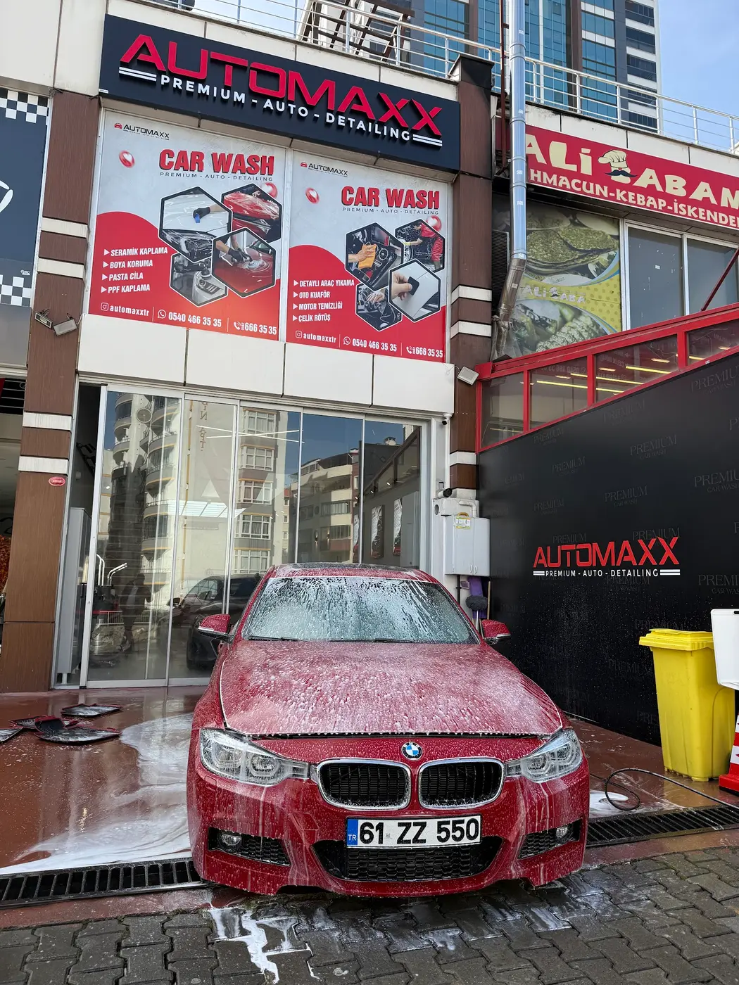 Automaxx dış cephesi: cam vitrin, hizmet panosu ve içeride bekleyen kırmızı araç