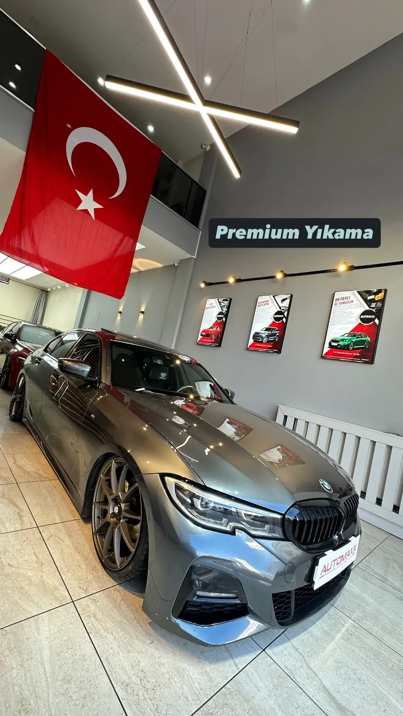 Automaxx showroomunda koyu renkli BMW; arka duvarda hizmet panoları ve “Premium Yıkama” tabelası