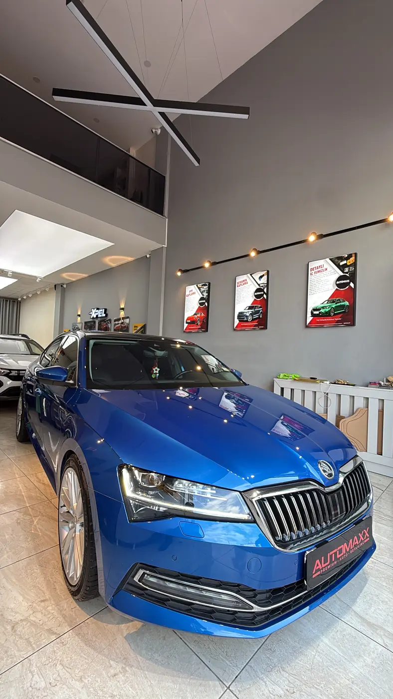 Automaxx showroomunda mavi araç; yanında ikinci araç ve hizmet panoları